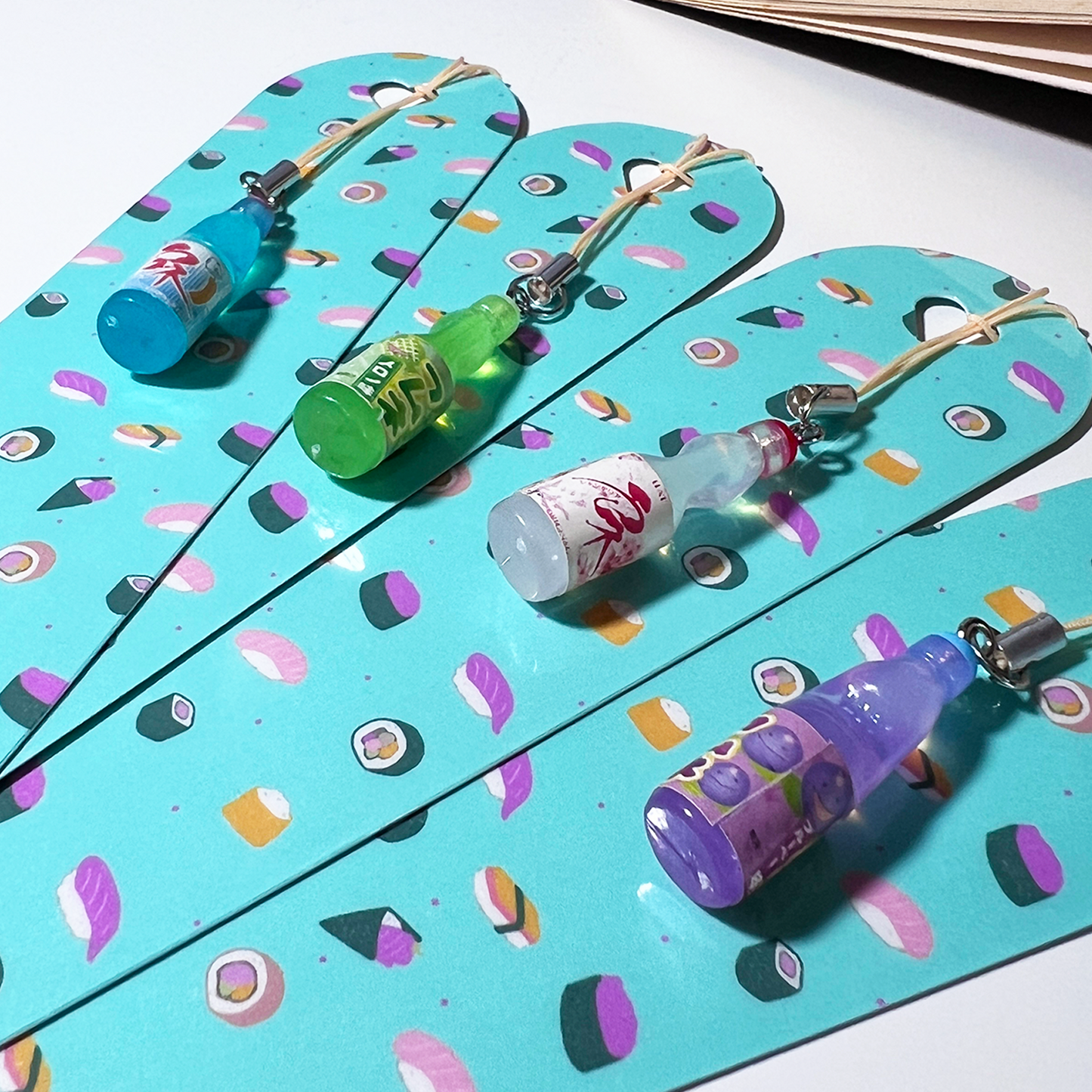 Turquoise sushi-patterned bookmark with a mini drink bottle charm resting on an open book.