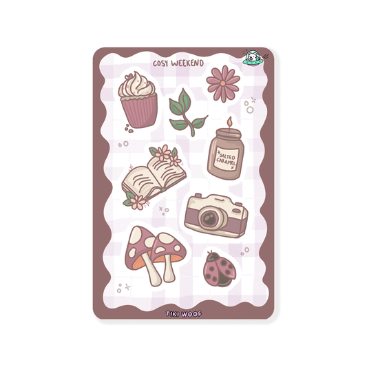 Mini sticker sheet featuring cosy weekend illustrations including a cupcake, candle, book, camera, mushrooms, flowers, and a ladybug in warm pastel brown and mauve tones.```