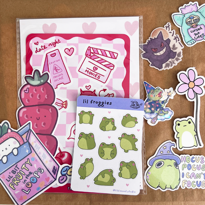 Close-up of Lucky Dip Lunch Bag label on brown paper bag surrounded by strawberry and frog vinyl stickers.
