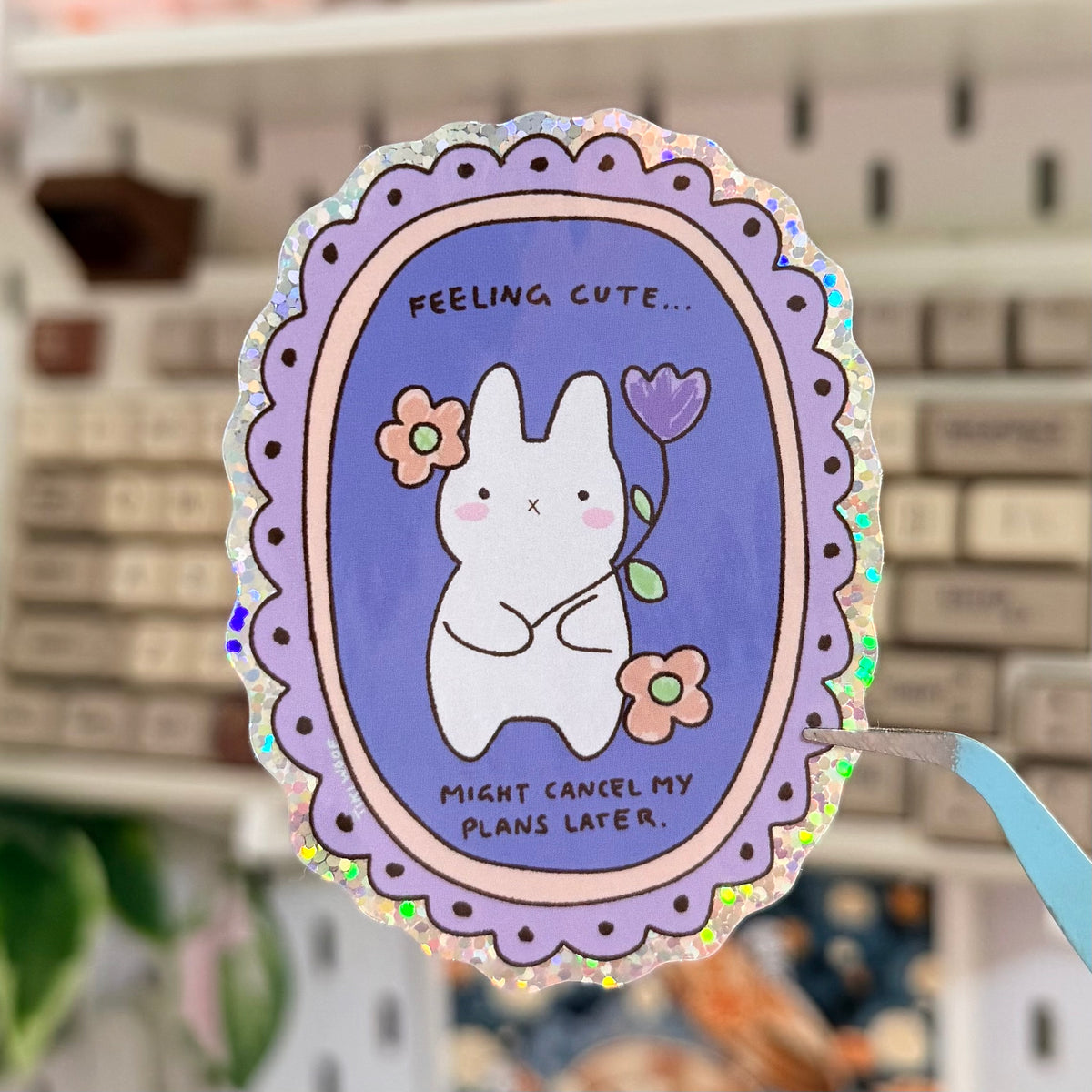 Feeling Cute Glitter Sticker featuring white and gray cat in a purple floral oval frame.