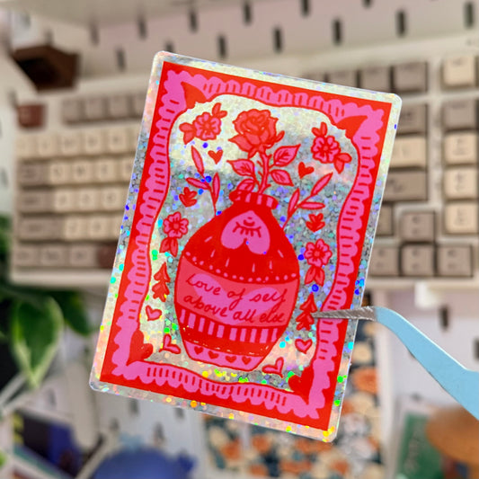 Above All Else Glitter Sticker featuring red and pink illustrated self-kindness card.