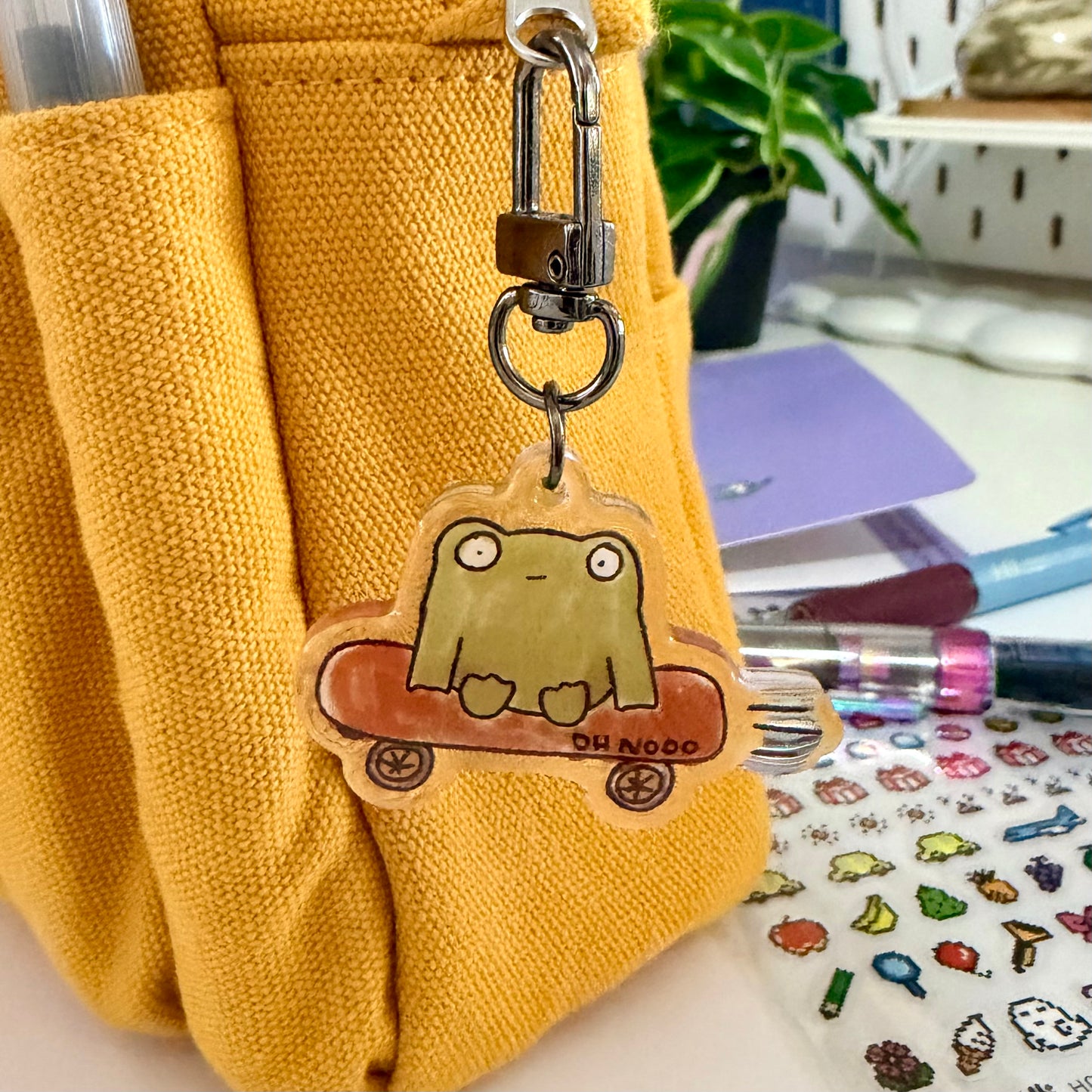 Keychain with a cartoon frog design attached to a yellow bag on a desk.