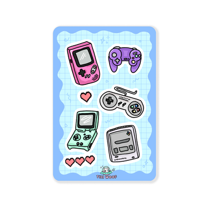 Sticker sheet featuring pastel retro gaming consoles, handhelds, and controllers on a blue grid background.```
