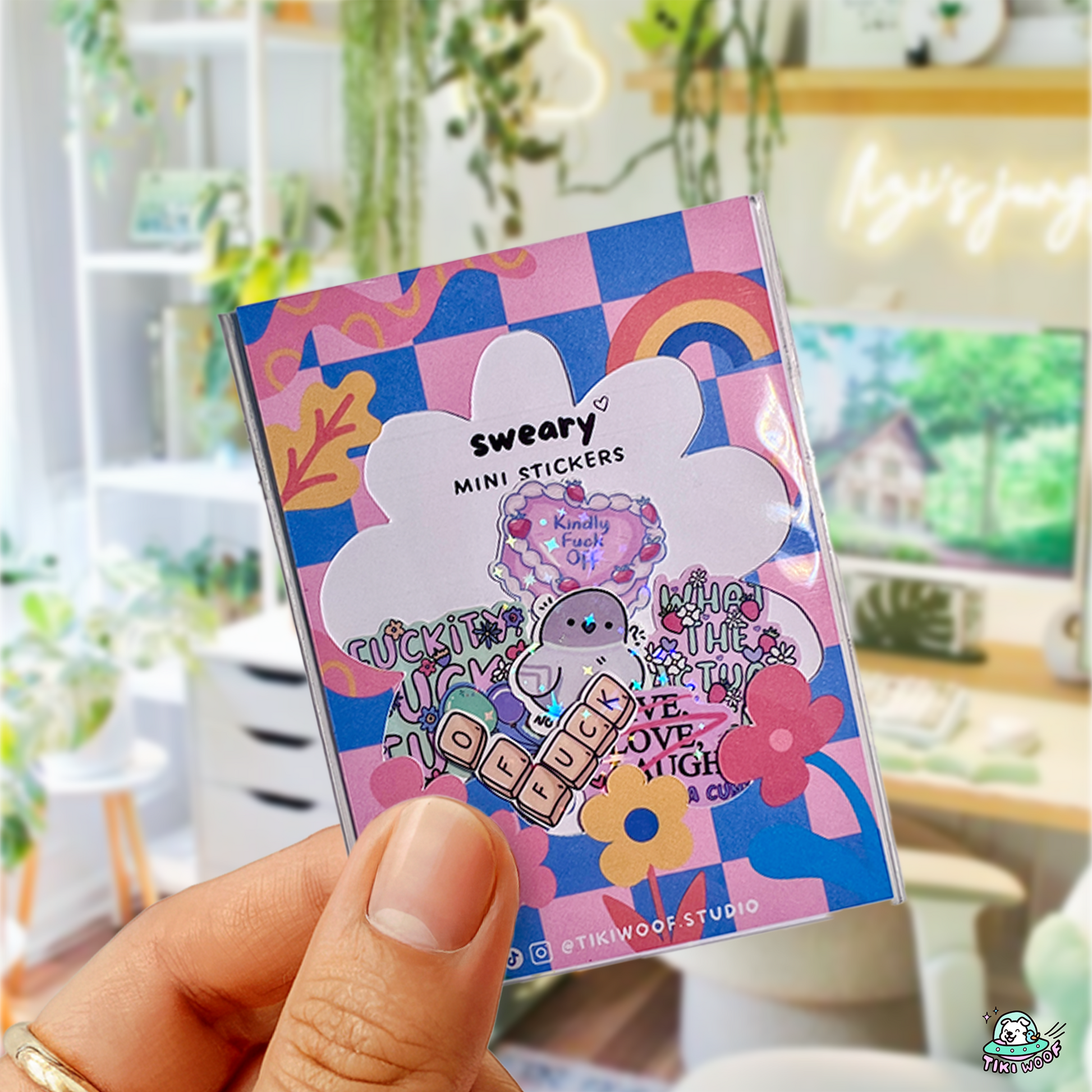 Hand holding a pastel Sweary Mini Sticker Pack featuring small profanity-themed stickers with flowers, rainbows, and a kawaii aesthetic.```