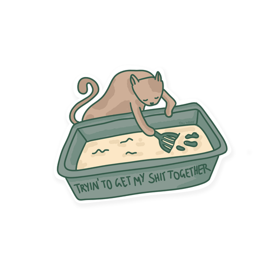 Funny sticker showing a cartoon cat cleaning a litter box with the words “Tryin’ to get my shit together” written on the front.```