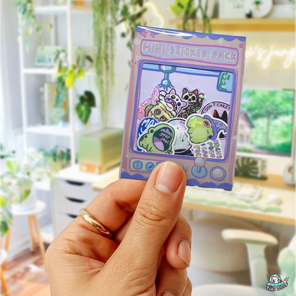 Hand holding a claw-machine-themed Froggy Friends Mini Sticker Pack featuring kawaii frog and cat vinyl stickers with positive sayings in pastel colours.```