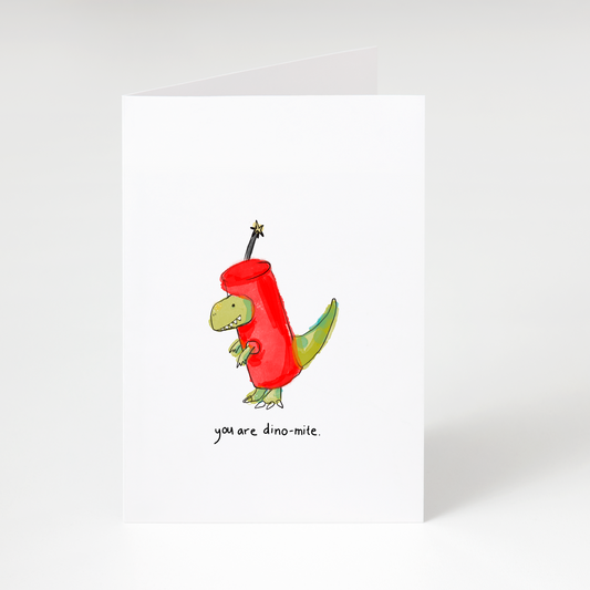Cute dinosaur wearing red dynamite costume with text “you are dino-mite” on white greeting card
